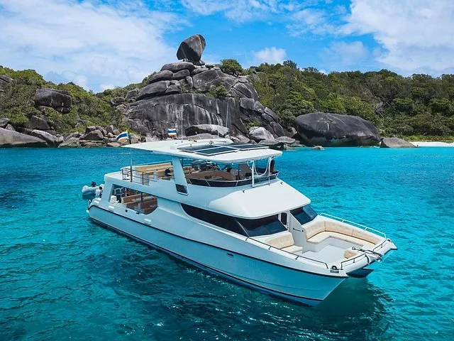 Catamaran boat anchored in clear water near rocky island coast