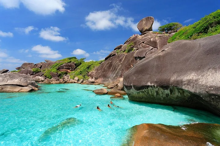 People swimming in clear turquoise water near large boulders